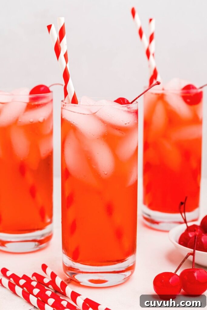 Bright red Shirley Temple drinks in tall glasses with straws and cherries. 