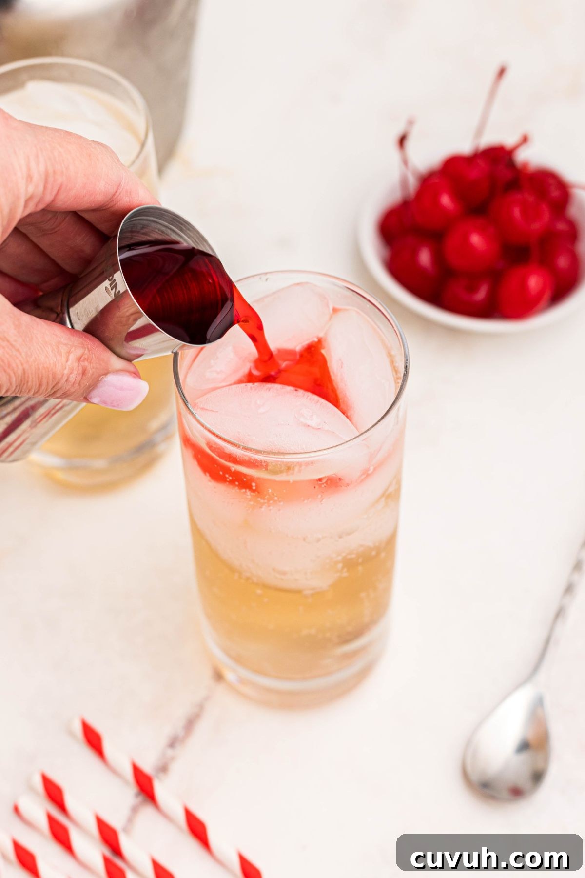 Red syrup mix being poured into a tall clear class filled with ginger ale and ice.