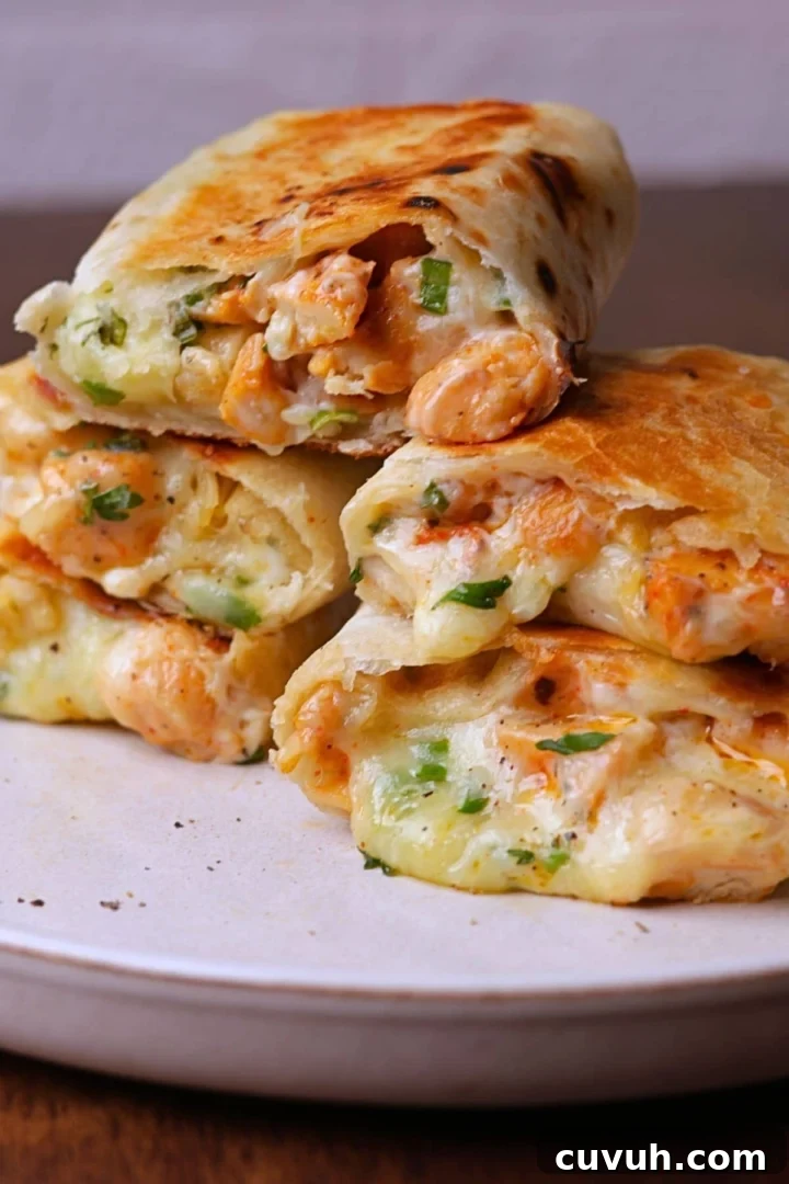Melty cheesy chicken wraps stack on a off white platter.