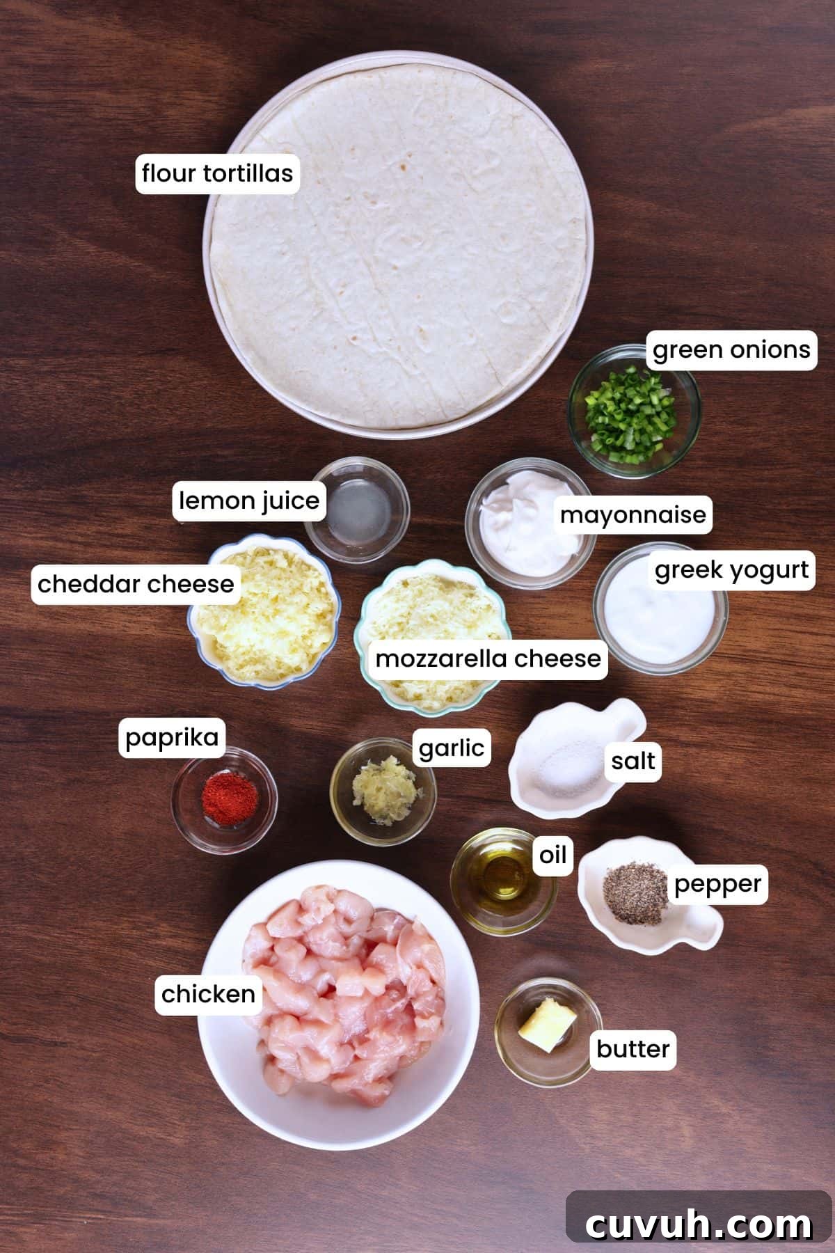 Flat lay of chicken, cheese, garlic, tortillas, and seasonings on a wooden surface.
