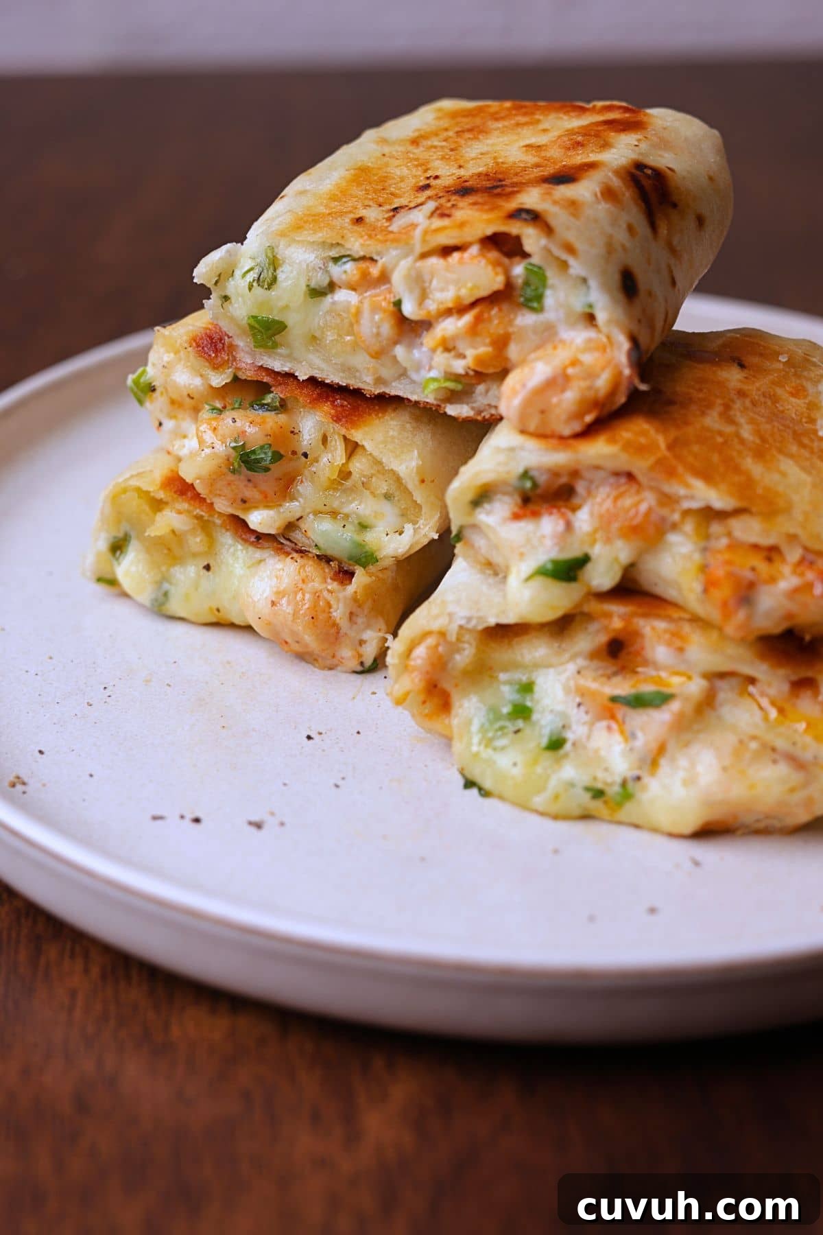 Cheesy chicken wraps stack on a off white platter.