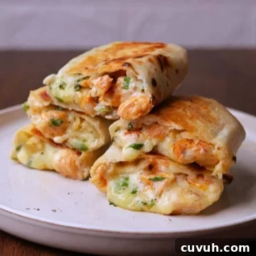 Stacked chicken wraps with melted cheese on a off white platter.