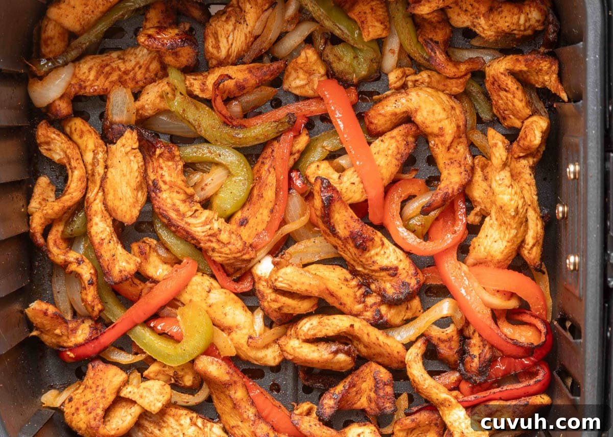 Crispy Air Fryer Chicken Fajitas with Peppers and Onions 11 Cooked chicken fajita strips, red and green bell peppers, and onions in an air fryer basket, lightly charred and ready to serve.