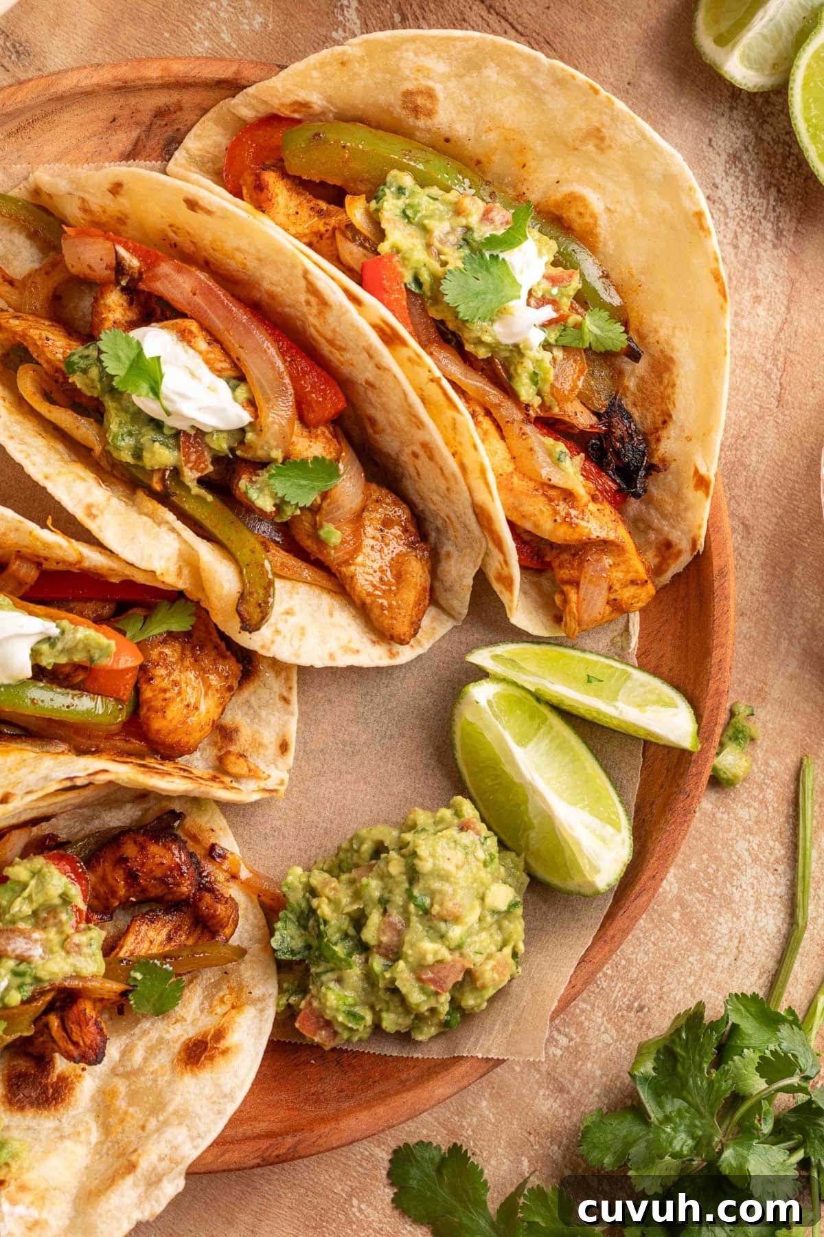 Crispy Air Fryer Chicken Fajitas with Peppers and Onions 13 Plated air fryer chicken fajita tacos in flour tortillas topped with guacamole, sour cream, and cilantro, served with lime wedges and extra guacamole on a wooden board.