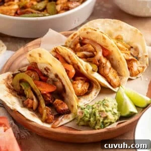 Four air fryer chicken fajita tacos in flour tortillas filled with seasoned chicken, sautéed peppers, and onions, served on a wooden plate with guacamole and lime wedges.