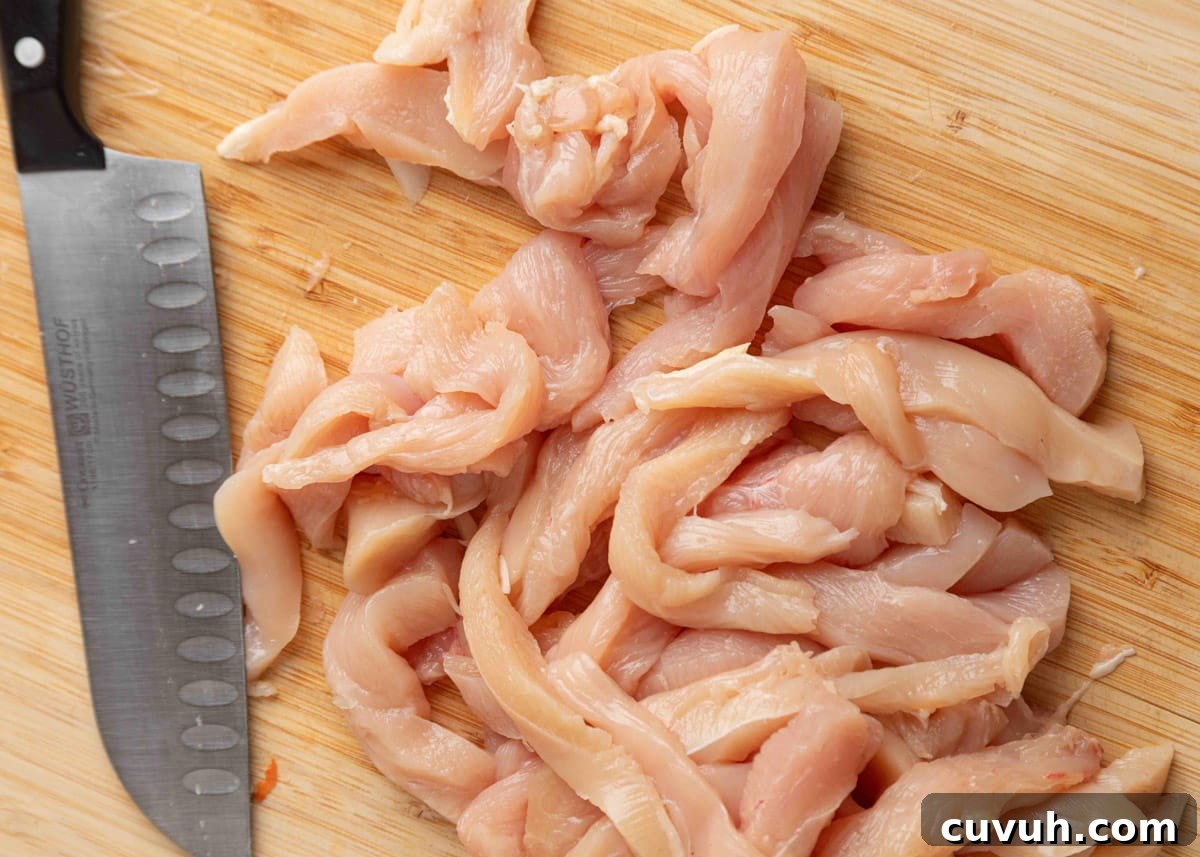 Crispy Air Fryer Chicken Fajitas with Peppers and Onions 4 Raw chicken breasts sliced into thin strips on a wooden cutting board with a chef’s knife, ready for fajita preparation.