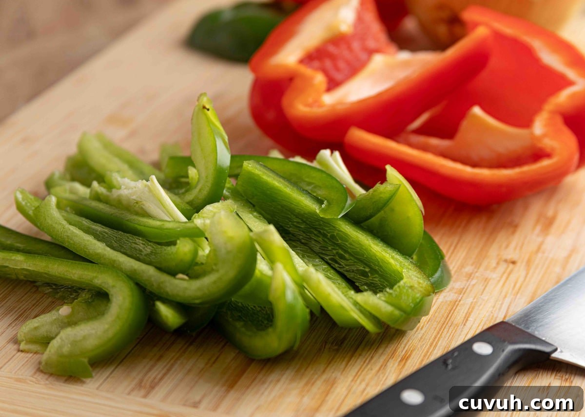 Crispy Air Fryer Chicken Fajitas with Peppers and Onions 5 Freshly sliced green bell peppers on a wooden cutting board with halved red peppers in the background and a paring knife nearby.