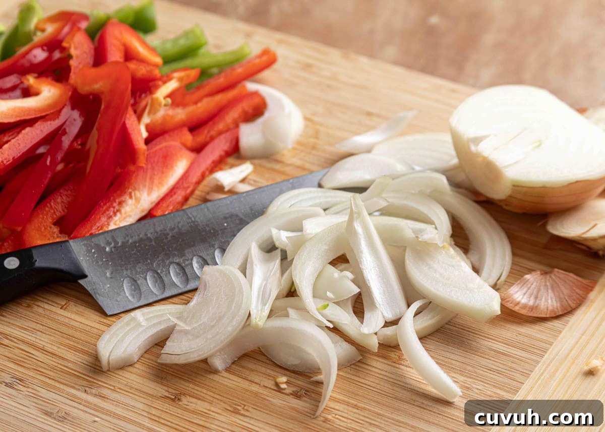 Crispy Air Fryer Chicken Fajitas with Peppers and Onions 6 Sliced yellow onions and red bell peppers on a wooden cutting board with a chef’s knife, ready to be cooked for chicken fajitas.