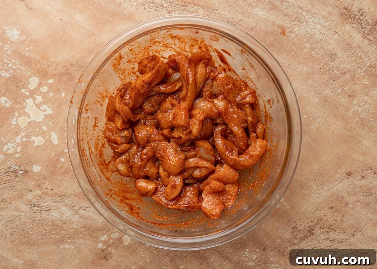 Crispy Air Fryer Chicken Fajitas with Peppers and Onions 8 Raw chicken strips coated in a seasoned marinade in a glass mixing bowl, ready to be cooked for fajitas.