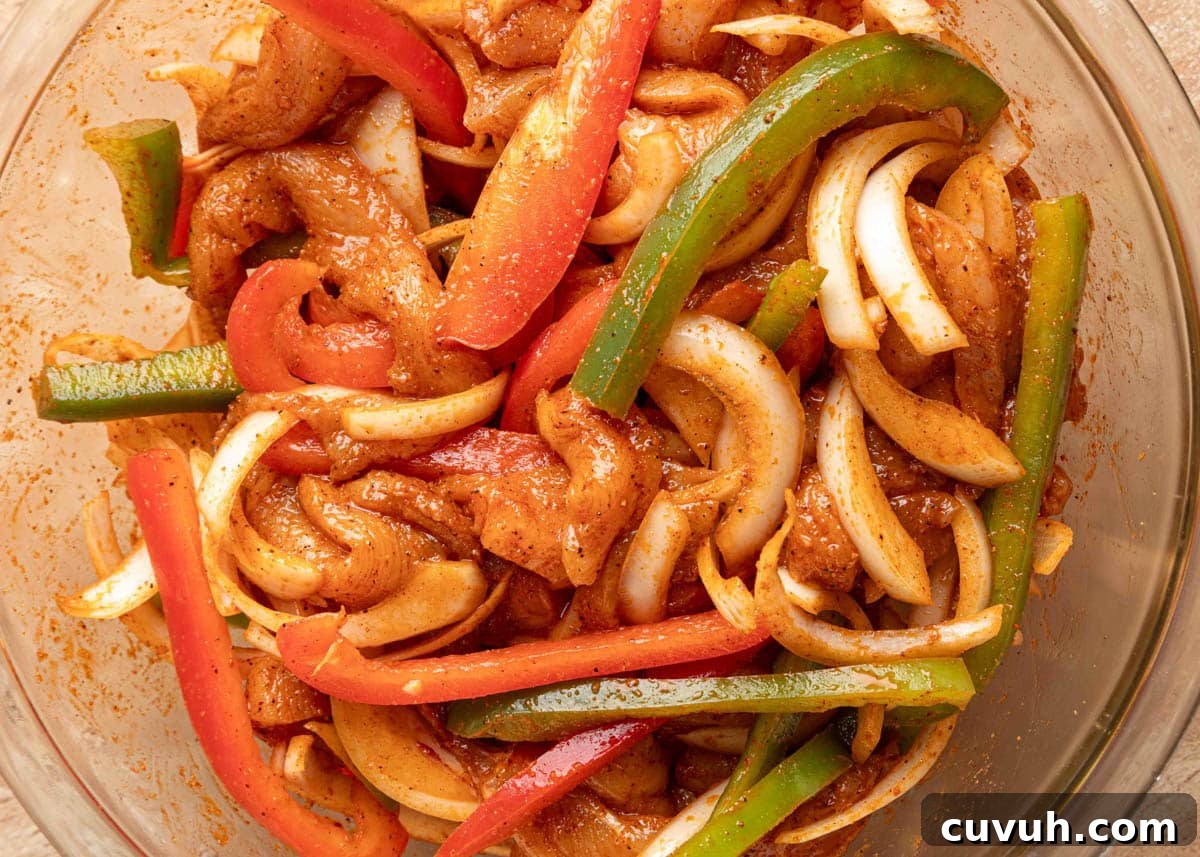 Crispy Air Fryer Chicken Fajitas with Peppers and Onions 9 Close-up of sliced raw chicken, red and green bell peppers, and onions coated in a seasoned marinade in a glass mixing bowl, ready to cook for fajitas.
