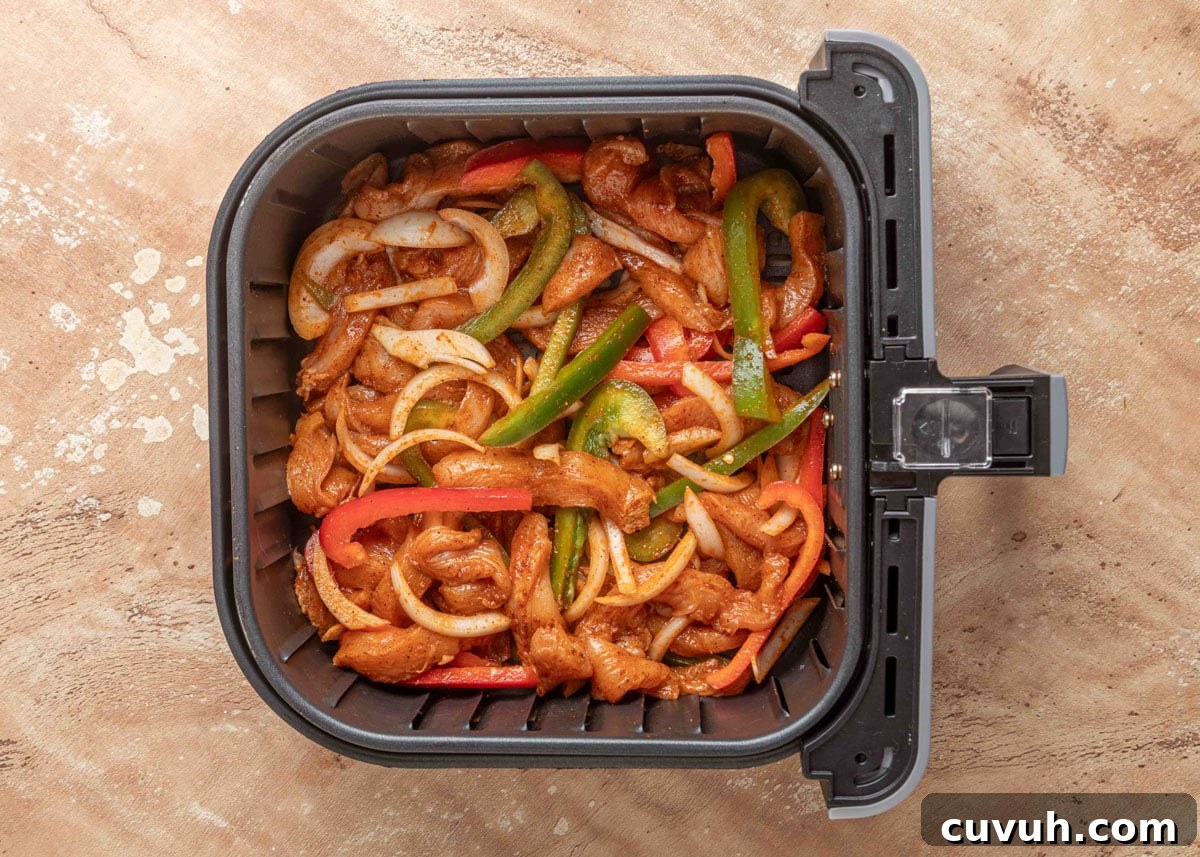 Crispy Air Fryer Chicken Fajitas with Peppers and Onions 10 Seasoned raw chicken strips, bell peppers, and onions arranged in a single layer in an air fryer basket, ready to cook for fajitas.