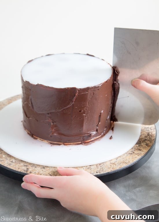 A metal scraper being used to scrape off the excess ganache as the turntable is turned.