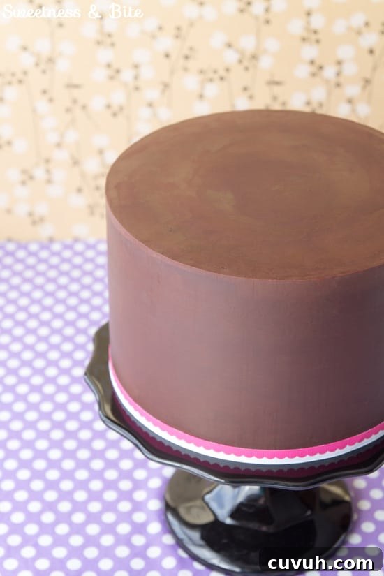 Close up of the finished ganached cake on a black cake stand with a pink and white ribbon around the base.
