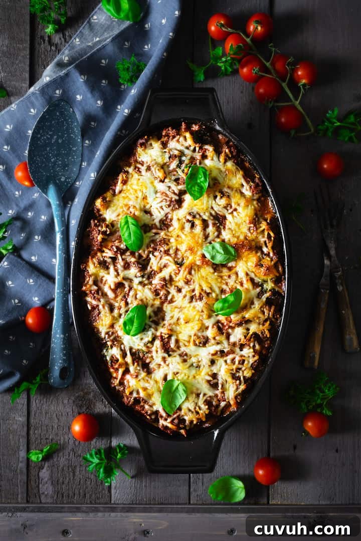 Ravioli lasagna in a black casserole dish on a gray wooden background with blue towel and tomatoes around.