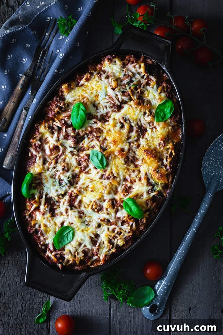 Black casserole dish with lasagna on a dark wood, sprinkled with basil leaves.