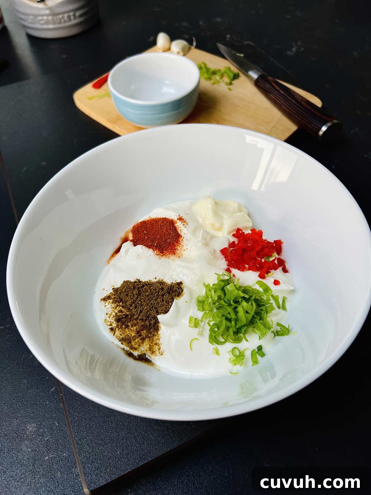 All the ingredients (sour cream, spices, scallions, Mayo, lemon juice) for a creamy sauce gathered in one white plate, ready to be mixed.