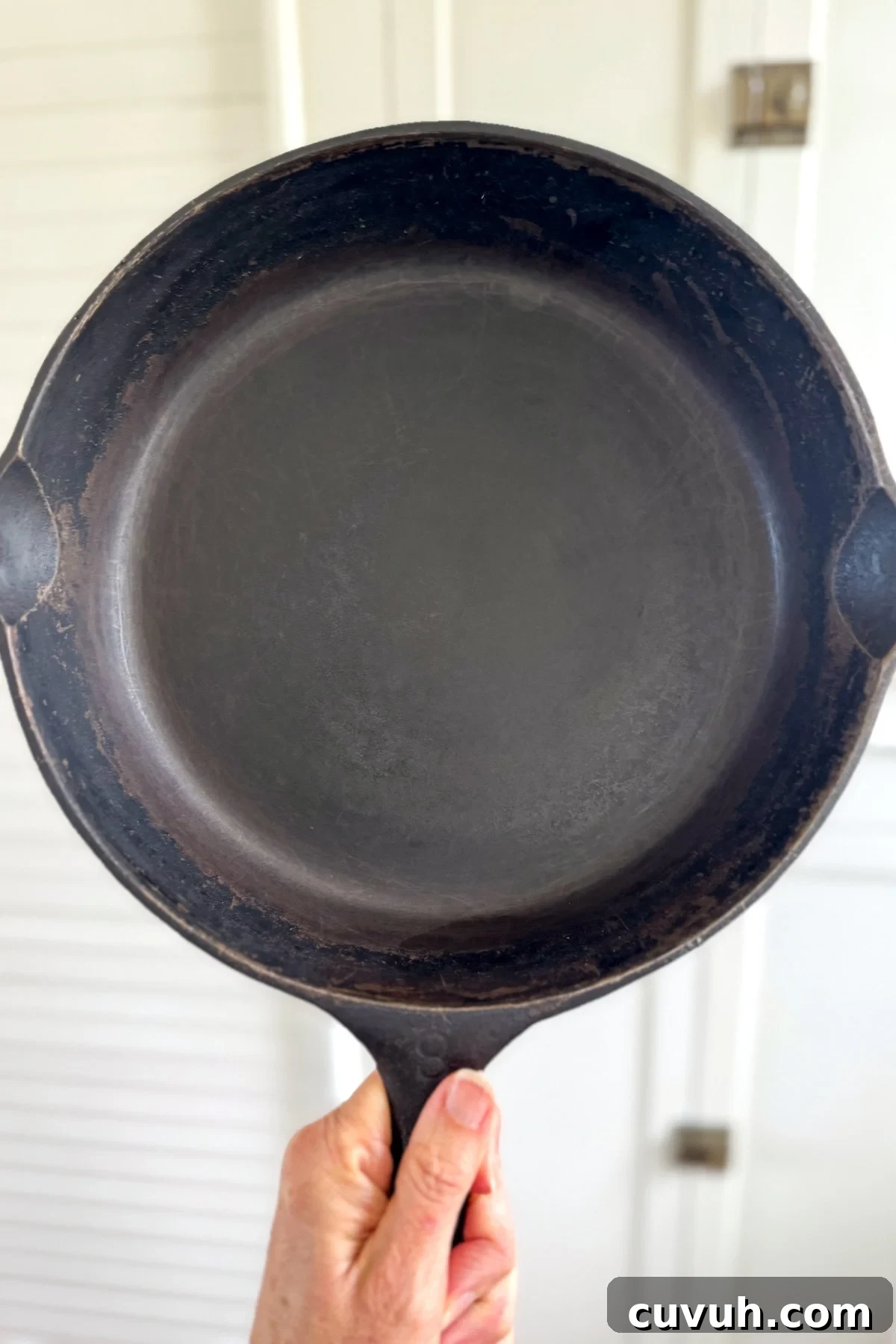 How to Clean and Care for a Cast Iron Skillet: Tips for Lasting Seasoning 2 holding clean cast iron pan in front of white cabinets