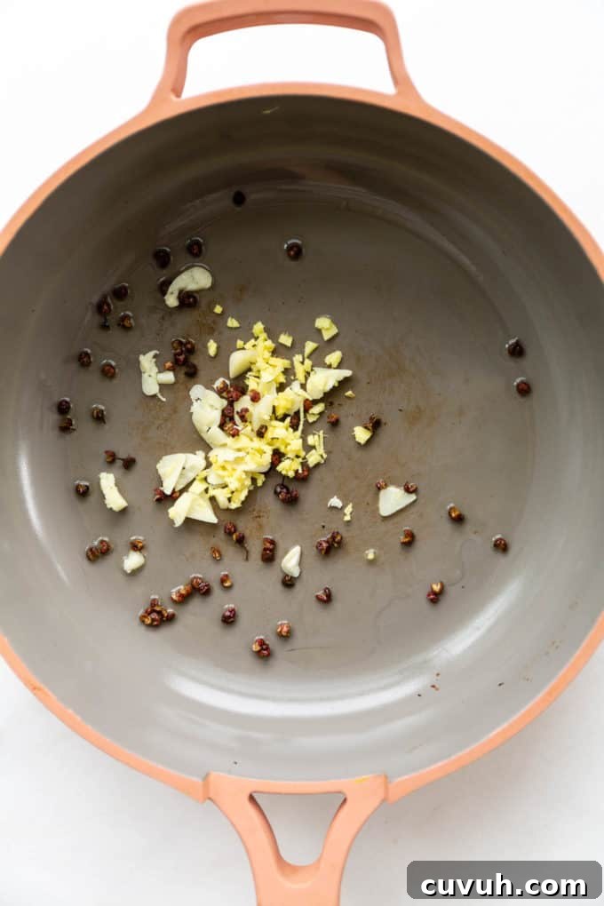 garlic, onions and sichuan peppercorns in a pink pan