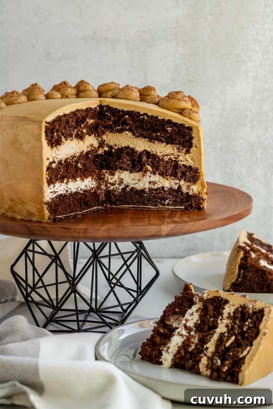 chocolate mocha cake cut open sitting on black metal and wood cake stand with 2 slices of cake on plate