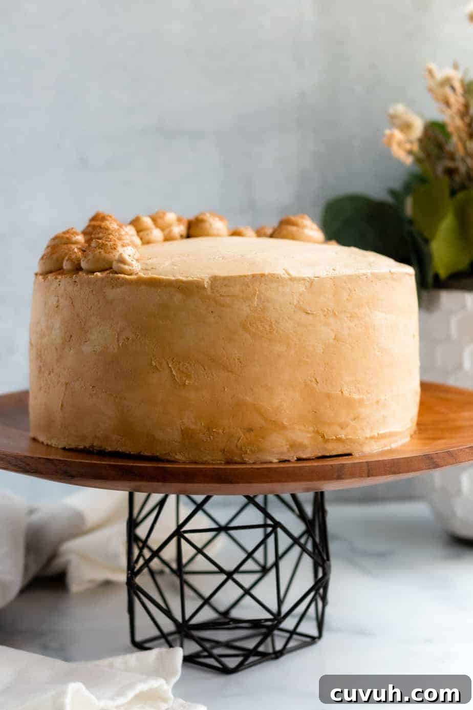 chocolate mocha cake on a wood and black metal cake stand with a white vase of flowers