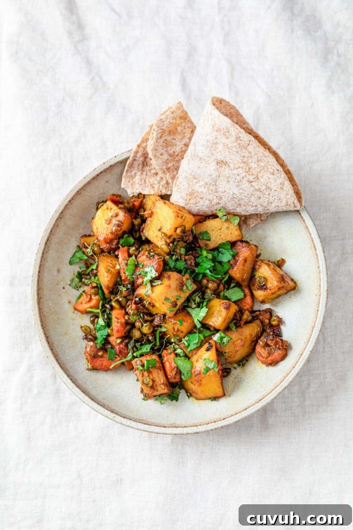 Mixed vegetable curry with potatoes, carrots, and peas in a bowl sprinkled with cilantro and served with roti.