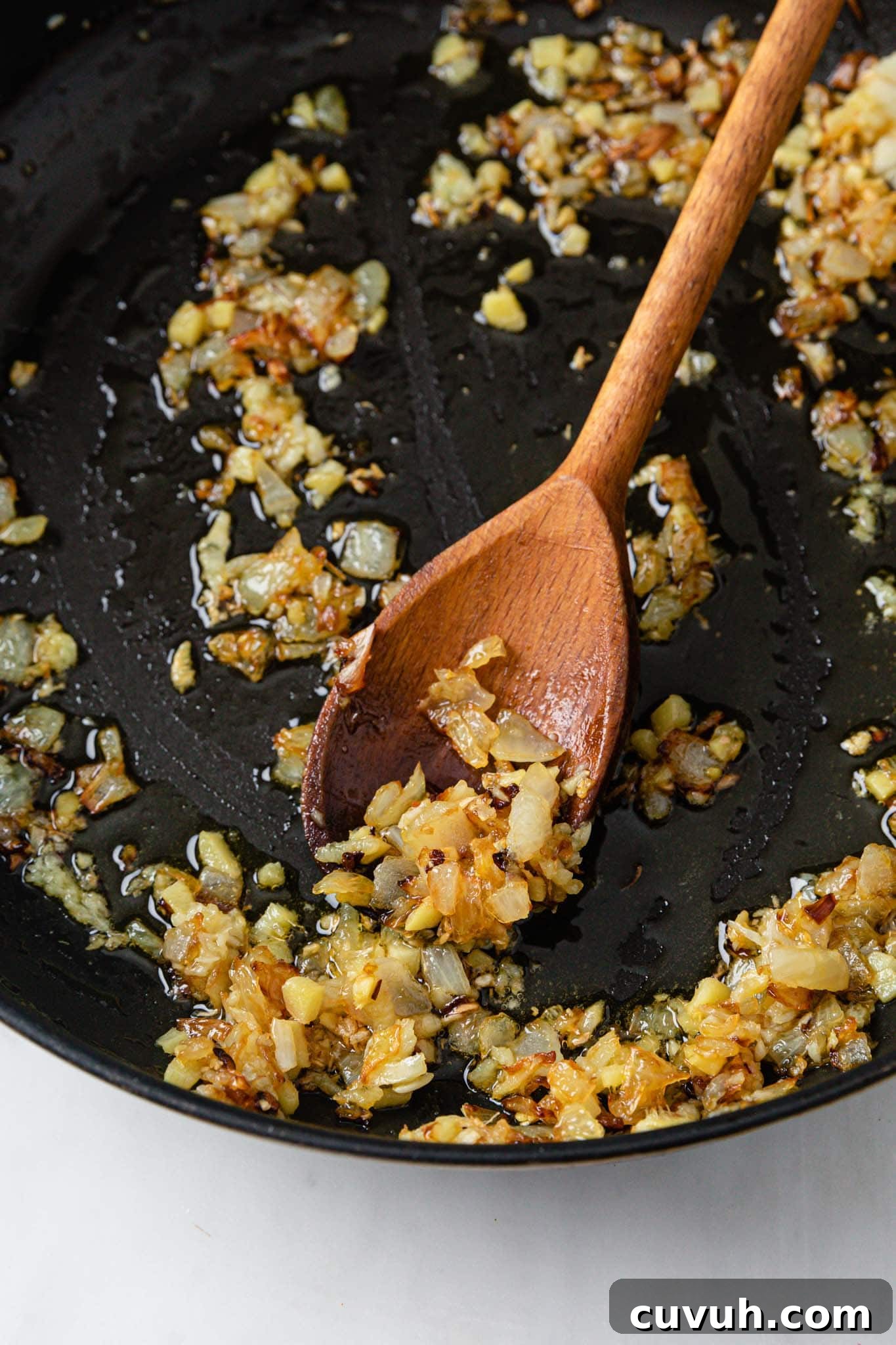 Sauteed onions with garlic and ginger in a black pan with a wooden spoon
