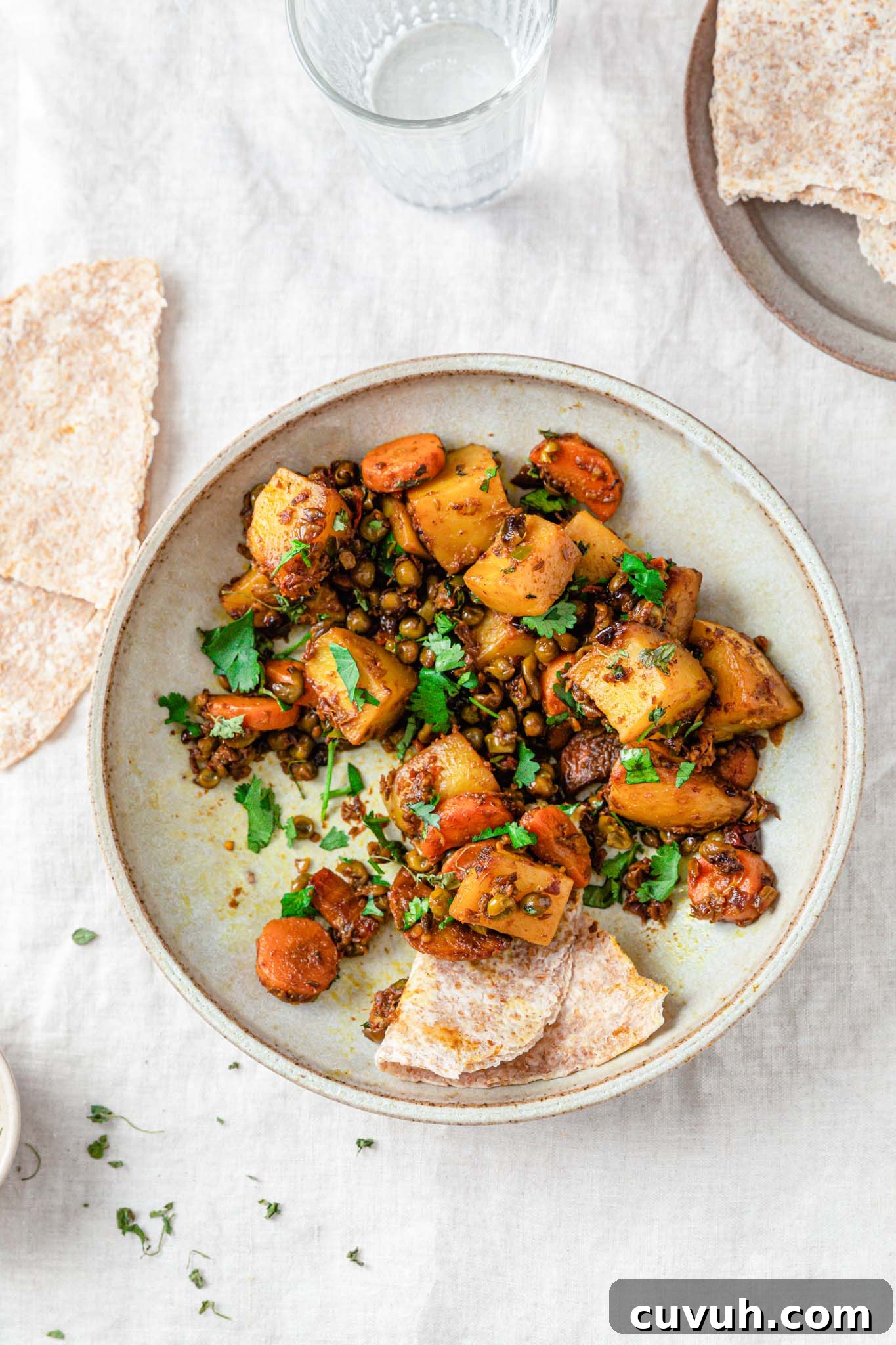 Curried mixed vegetables in a bowl with bread and a glass of water on the side