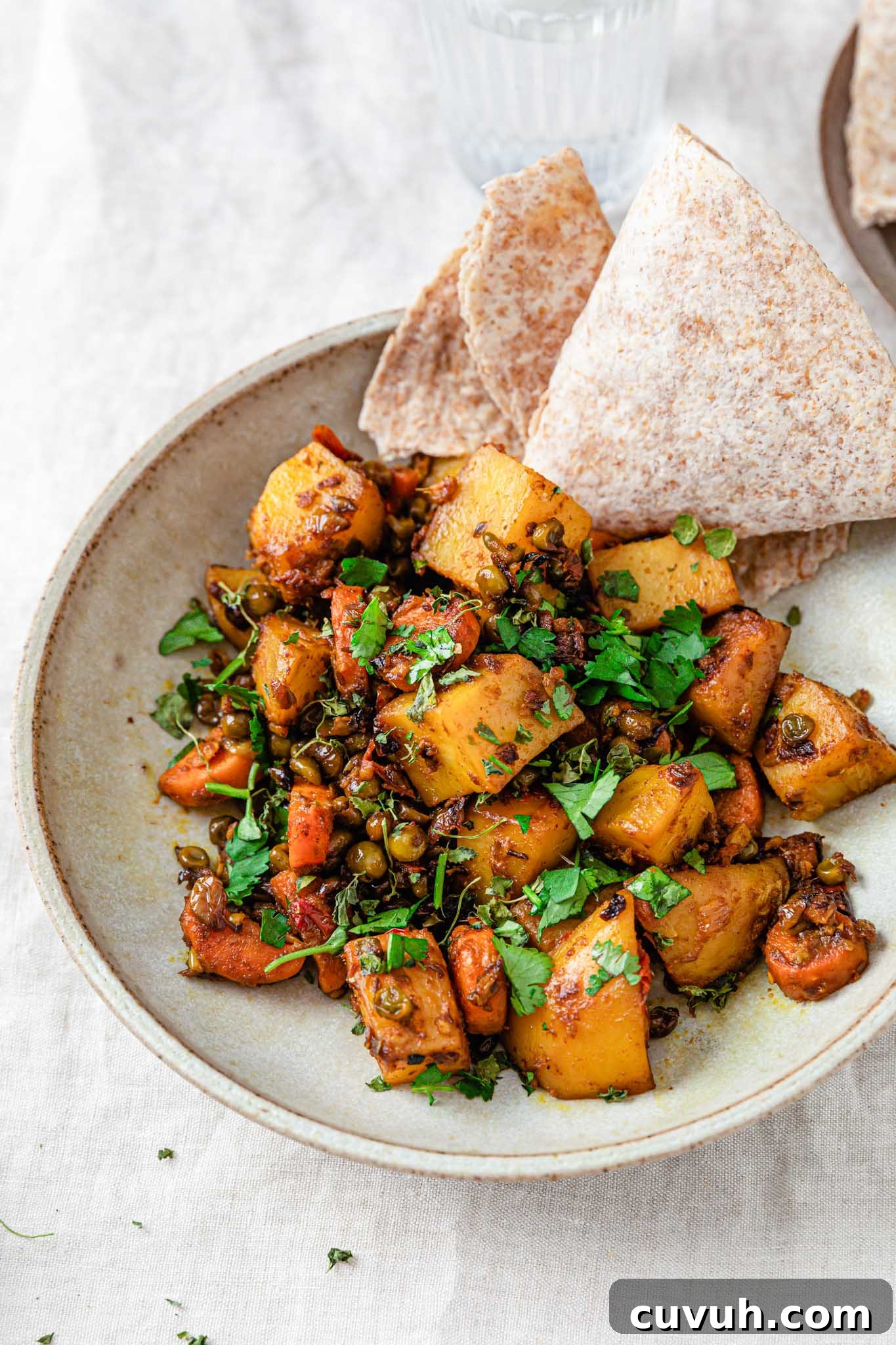 Potatoes, carrots, and in a beige bowl with a piece of roti on the side.