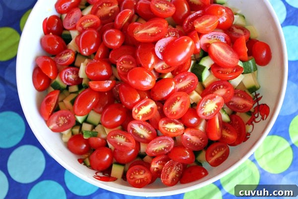 Tomatoes tomato added to a bowl of zucchini and corn set on a blue and green polka dot tablecloth