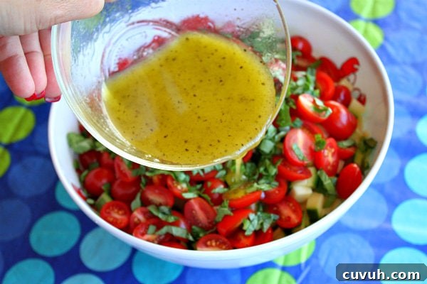 Honey Lime Vinaigrette hand pouring dressing into bowl of fresh corn, zucchini and tomato salad, set on a blue and green polka dot tablecloth