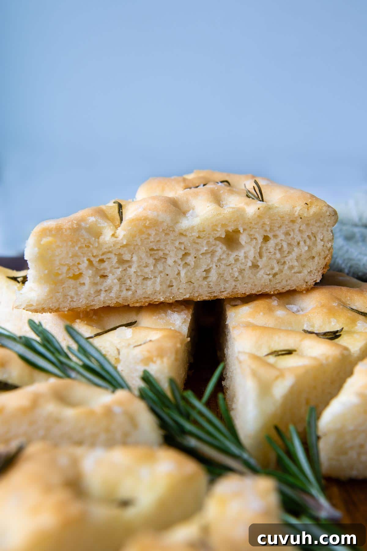 a slice of focaccia resting on other slices with fresh rosemary under