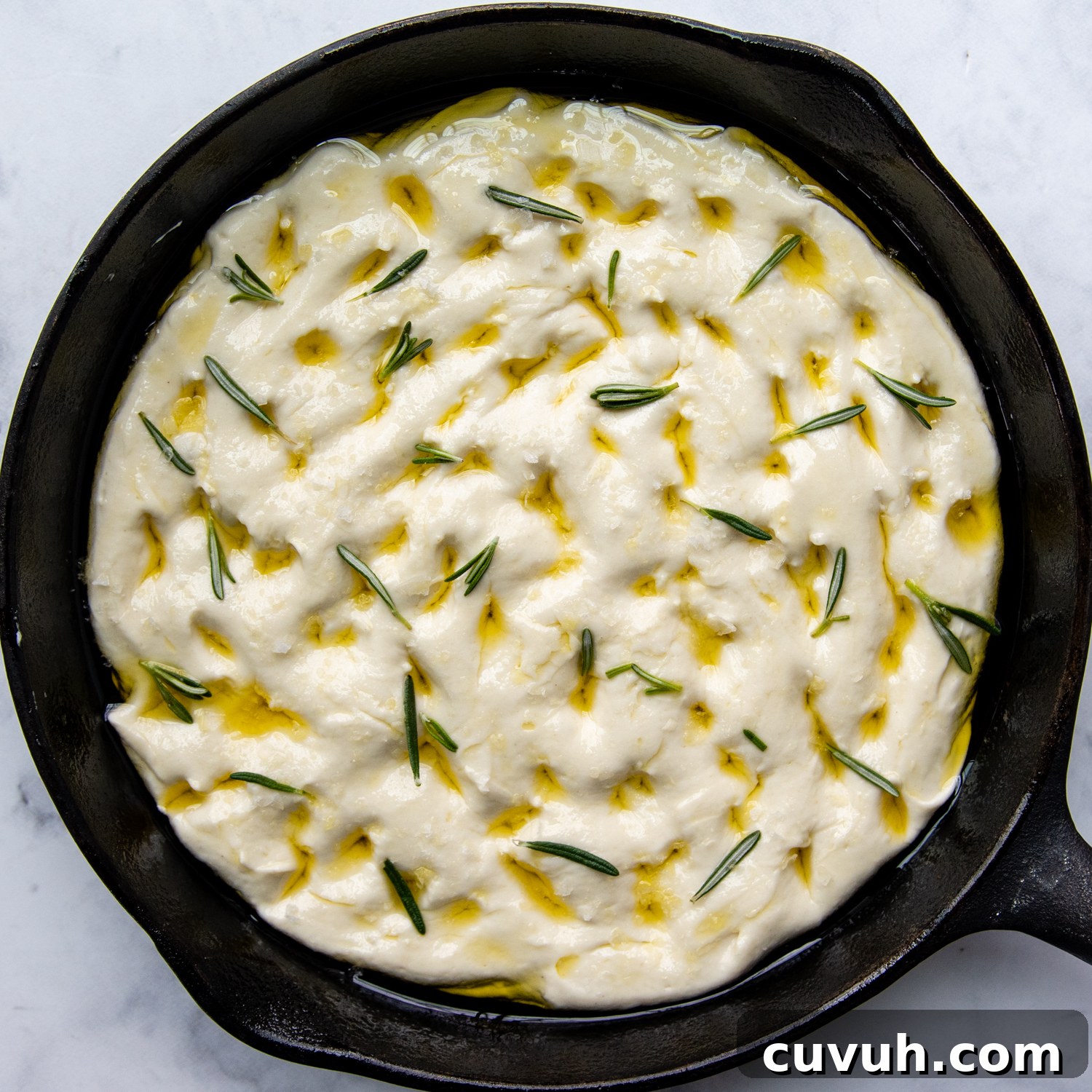 unbaked focaccia with oil and rosemary on top.