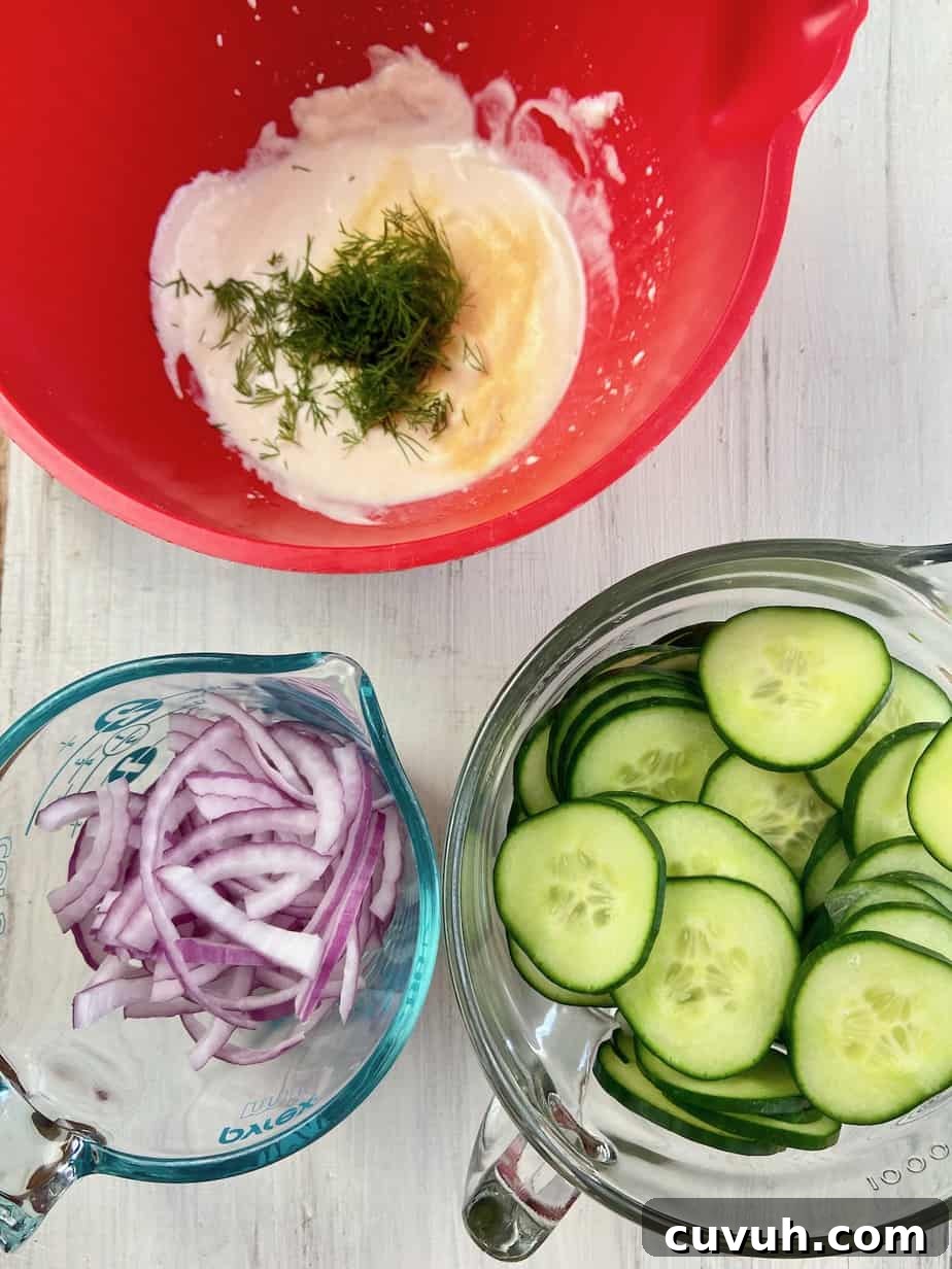 A bowl of sliced cucumbers, a bowl of sliced onions and a red bowl with the dressing ingredients.