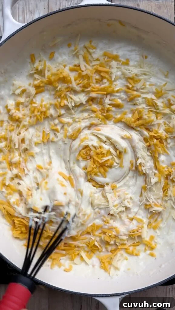 Creamy Baked Macaroni and Cheese Casserole 8 Grated cheese being stirred into a pan full of creamy sauce.