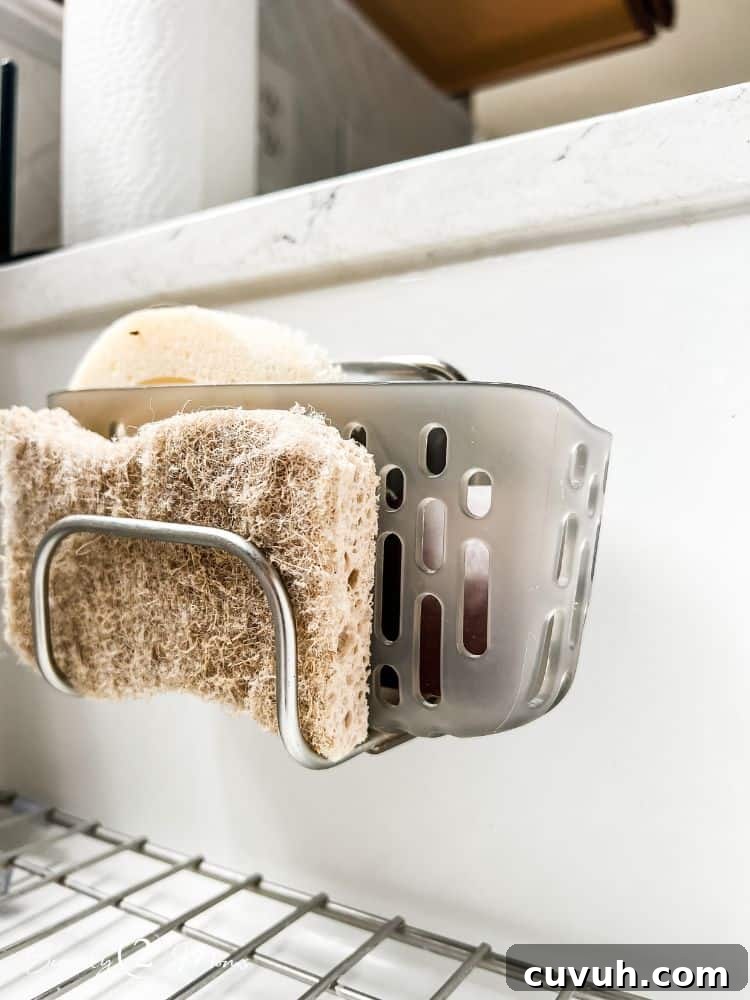 OXO suction cup sink caddy mounted inside a white fireclay sink holding a sponge.