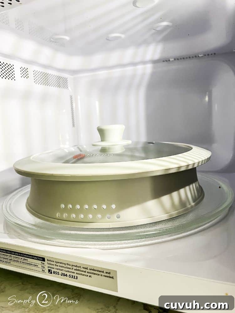 Silicone and glass splatter cover with vents on the sides and a knob handle inside a microwave