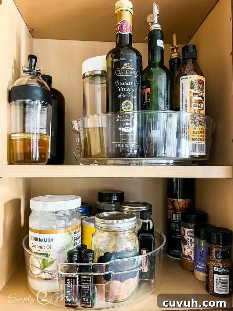 Two cabinet shelves each with clear plastic lazy Susan organizers holding oils, vinegars, and seasonings.
