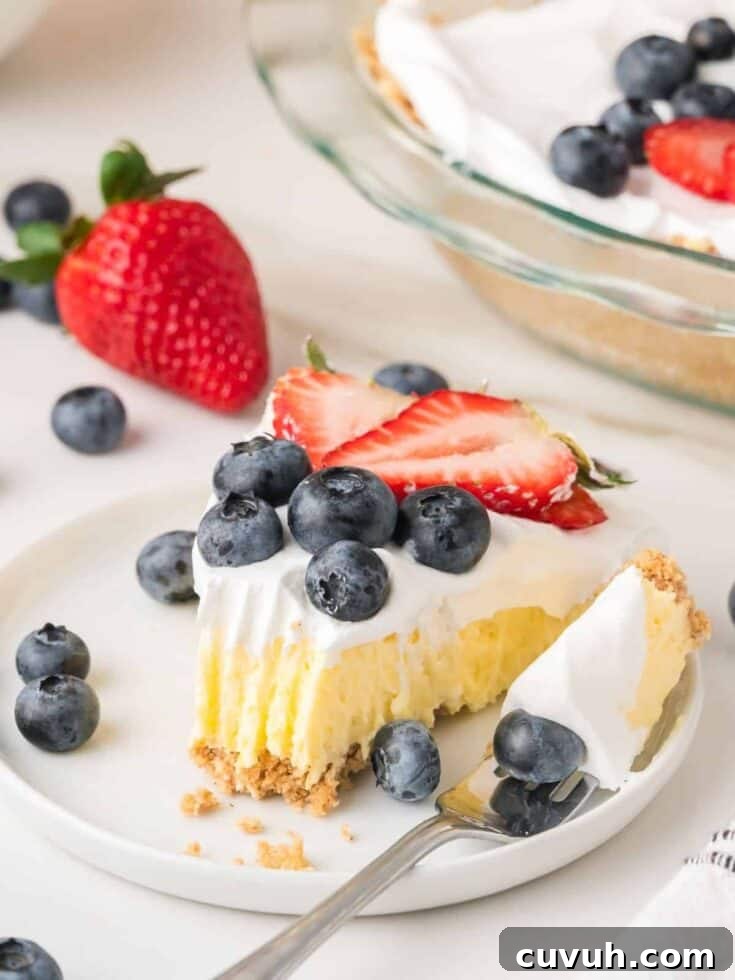 Slice of vanilla pudding pie on a white plate, garnished with berries. A fork has cut out a bite of the cream pie.