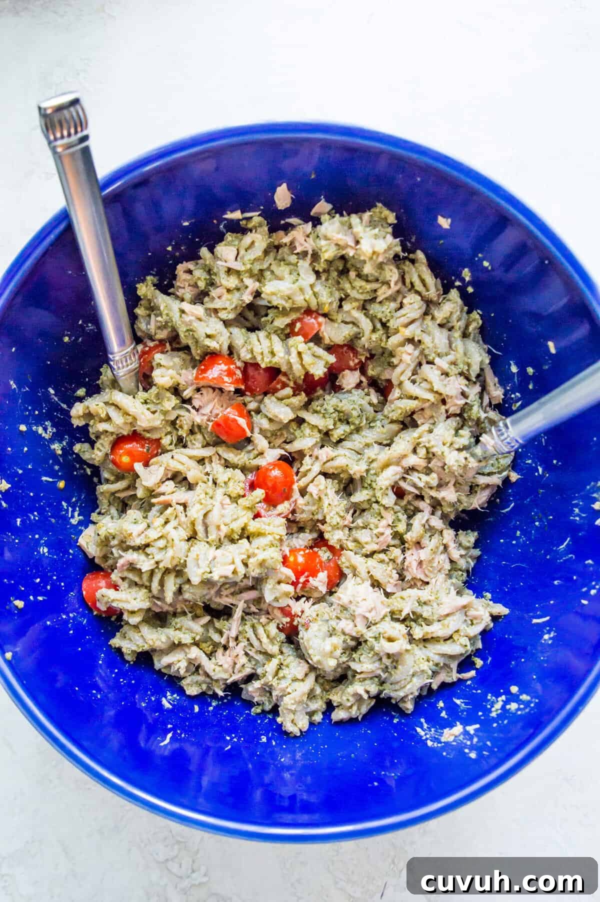 4-Ingredient Tuna Pesto Pasta Recipe – Ready in Minutes 7 A bowl filled with cooked noodles covered in pesto sauce with chopped tomatoes on it.