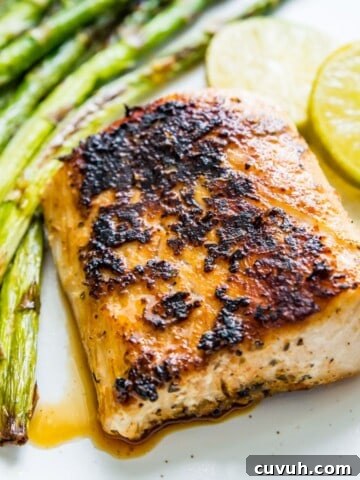 A piece of blackened mahi mahi on a plate with cooked asparagus and lime wedges beside it.
