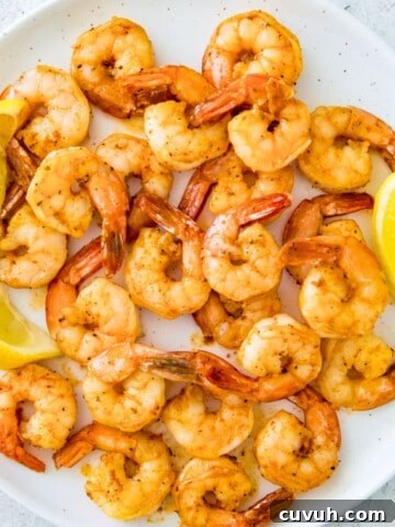 A plate with pan seared shrimp on it with lemon wedges beside them.