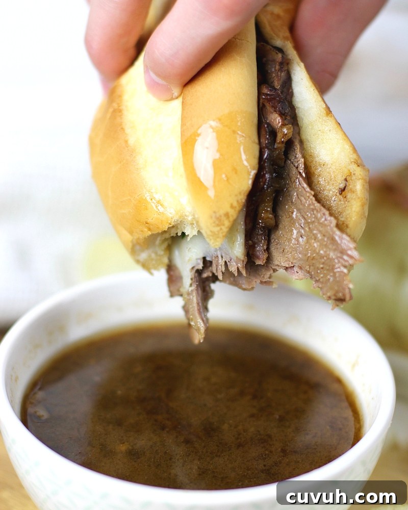 Slow-Cooker French Dip Sandwich Recipe with Juicy Beef and Au Jus 3 French Dip Sandwich being dipped in the au jus sauce.