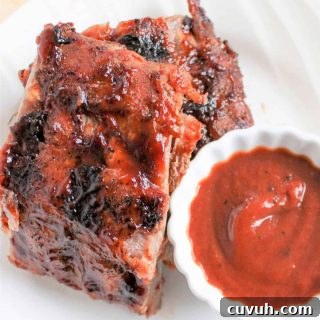 Closeup image of juicy grilled ribs served on a white plate with a side of barbeque sauce for dipping.