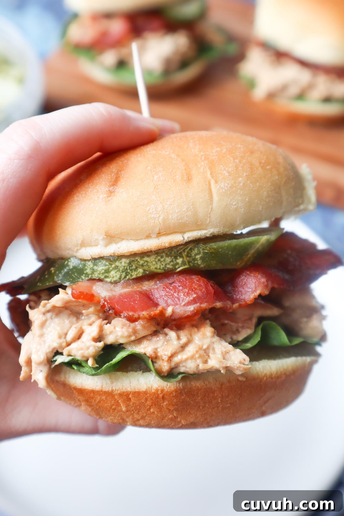 Smoked Gouda Chicken Bacon Ranch Sandwich Recipe 2 hand holding a chicken bacon ranch sandwich with ranch shredded chicken, lettuce, bacon, and pickle