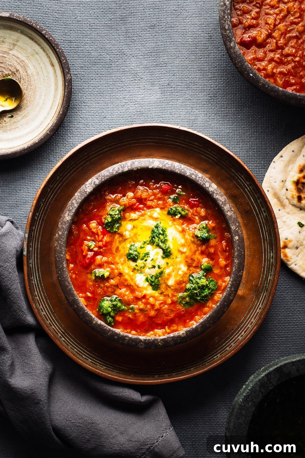 Bowls of bright red lentil soup viewed from above on a dark grey background.