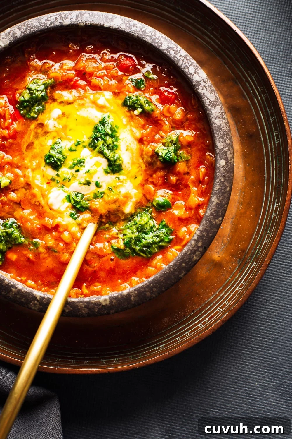 A bowl of red lentil soup with yoghurt and green chilli salsa and a gold spoon.