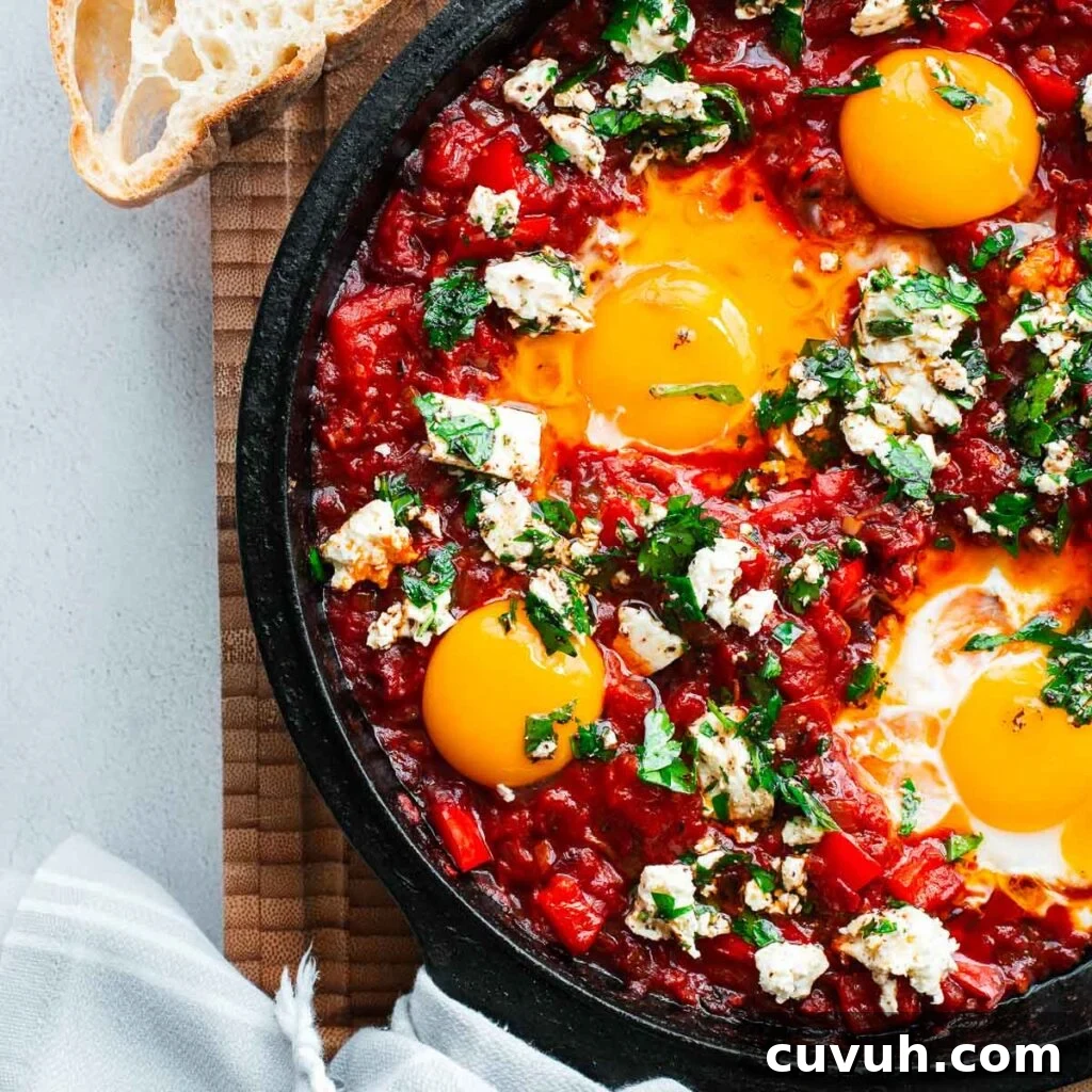 Harissa shakshuka with bright red roasted pepper sauce with soft-cooked eggs and visibly runny yolks topped with feta and parsley in a cast-iron skillet.