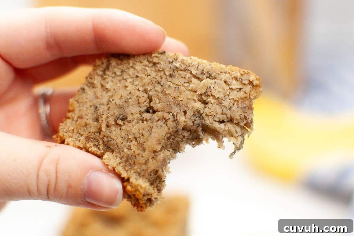 A hand holding a partially bitten slice of banana bread.