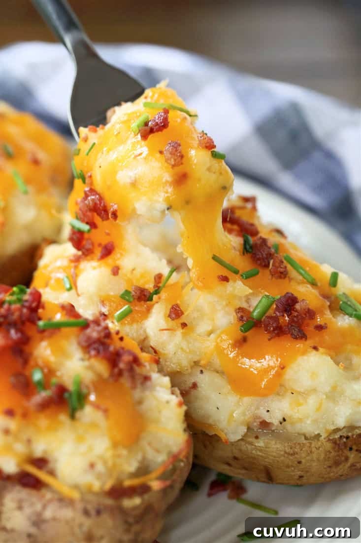 Twice Baked Potatoes are a delicious side dish that can be totally made ahead of time! Creamy, cheesy potato filling in a crispy baked skin! A fork taking a bite of a twice baked potato