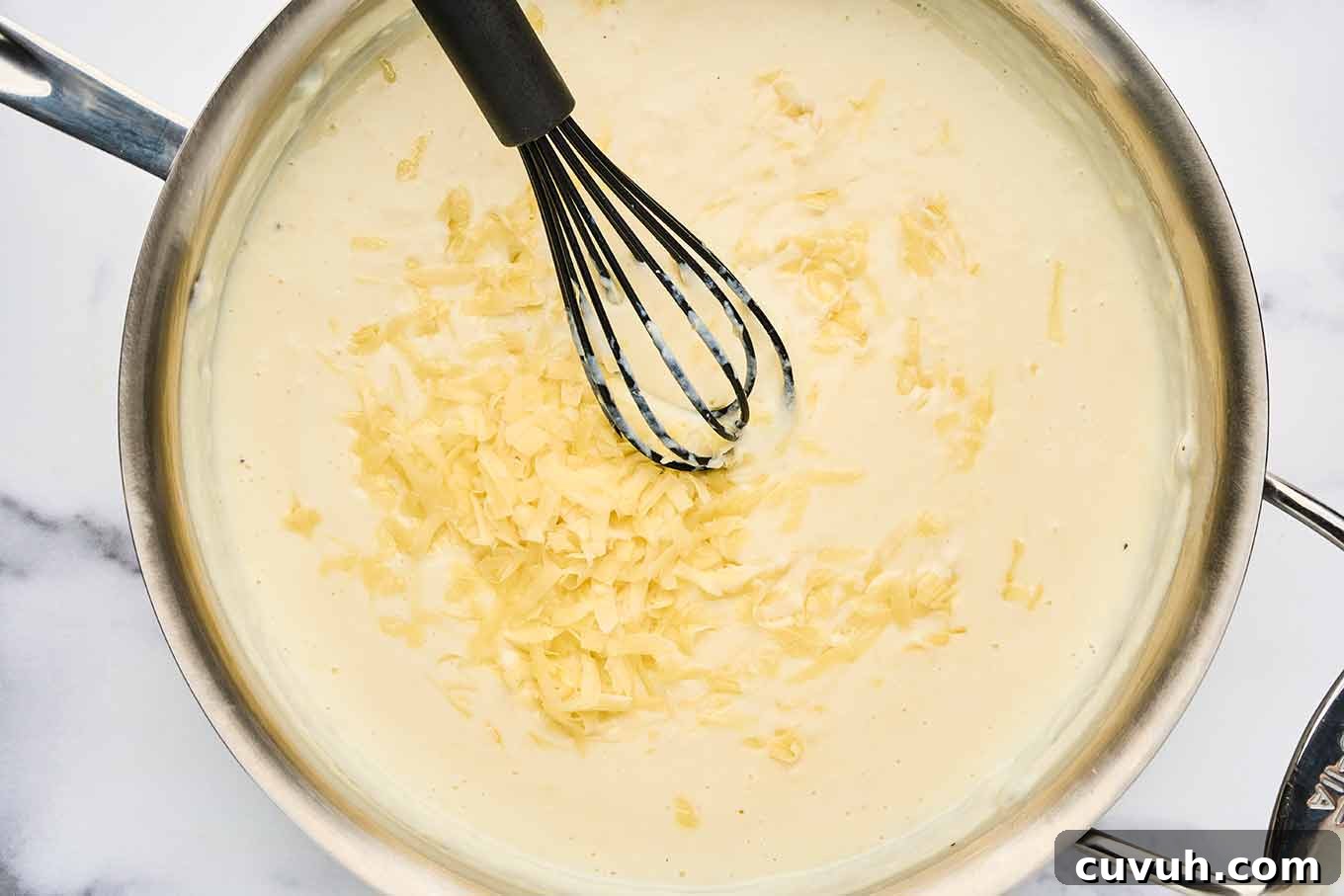 Coarsely grated cheese being stirred into bechamel for homemade macaroni and cheese.